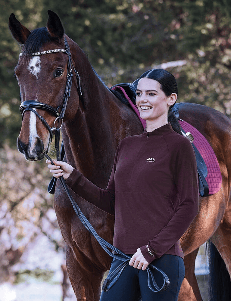 Woman stood with horse wearing weatherbeeta bamboo long sleeve performance base layer in mulberry