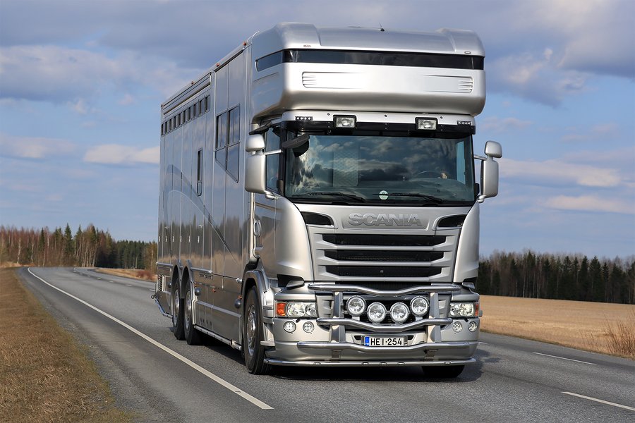 big silver horsebox being driven on a road